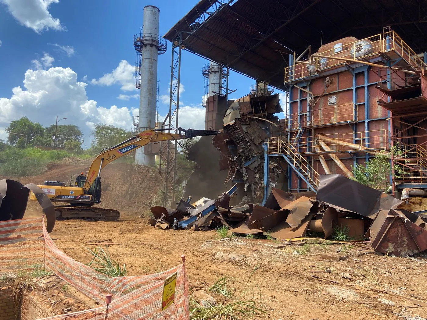 Escavadeira no desmonte de caldeira em planta industrial desativada
