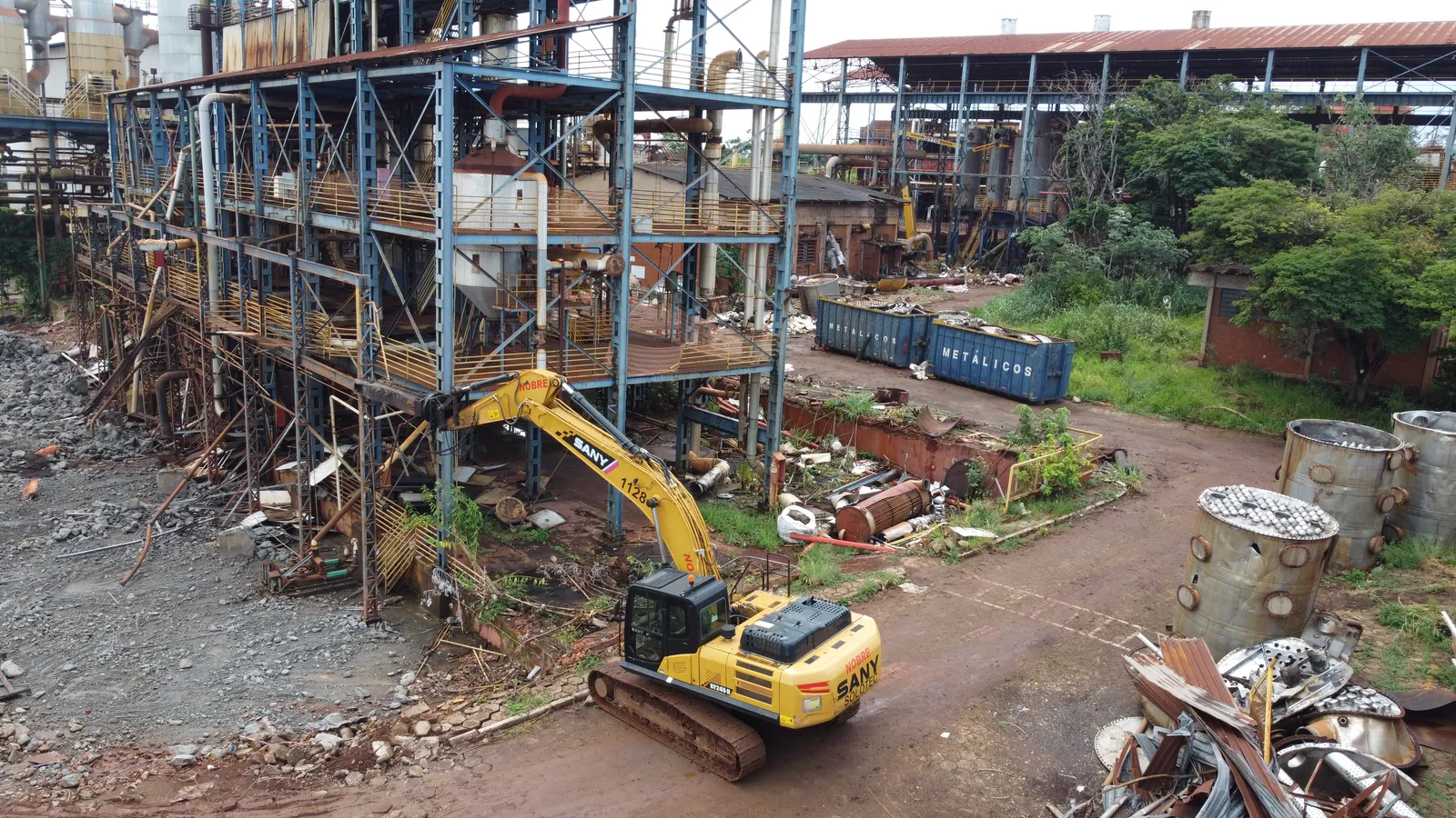 Escavadeira entre estruturas metálicas em desmonte, vista aérea